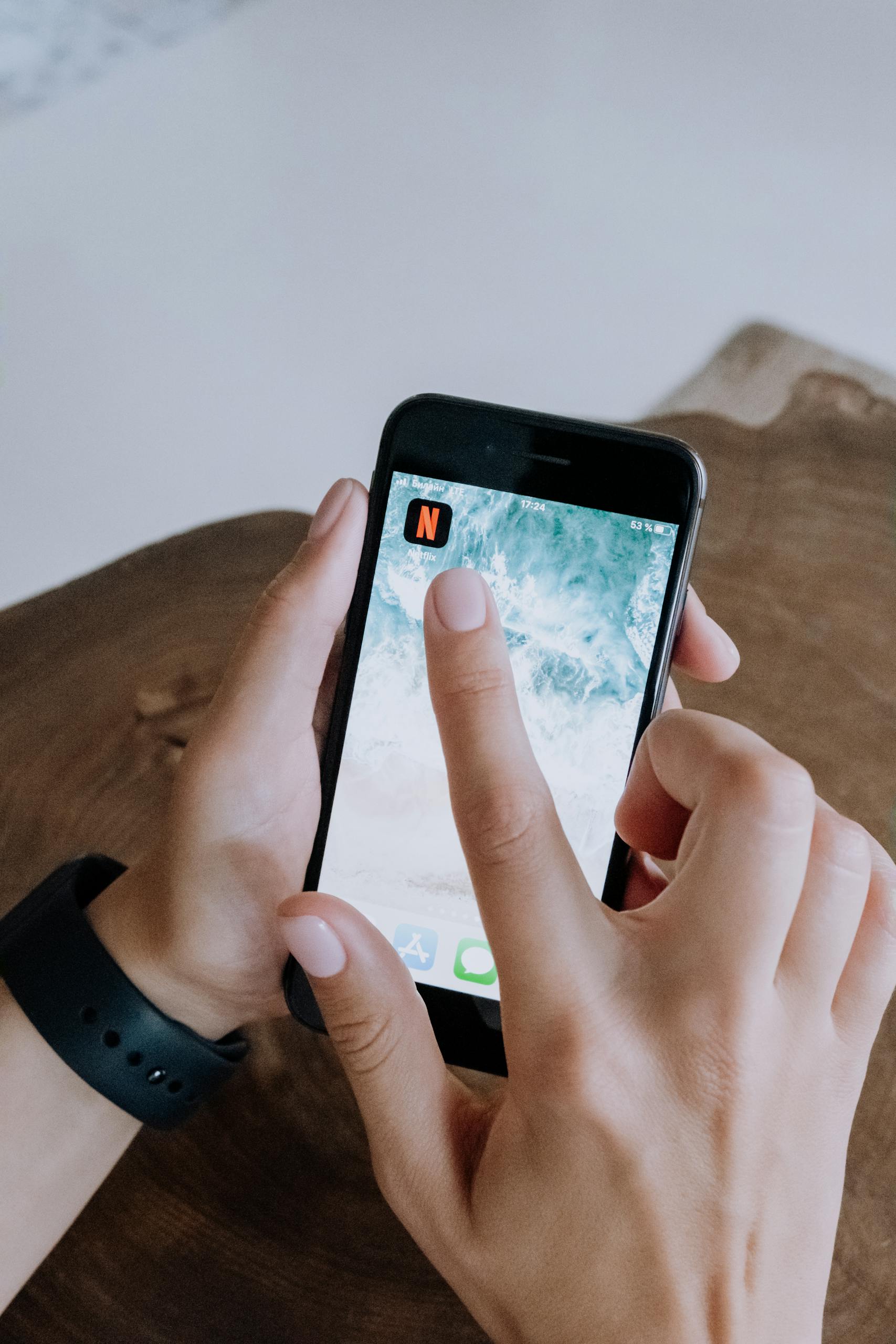 Close-up of hands using a smartphone app on a wooden table, depicting modern technology and connectivity.